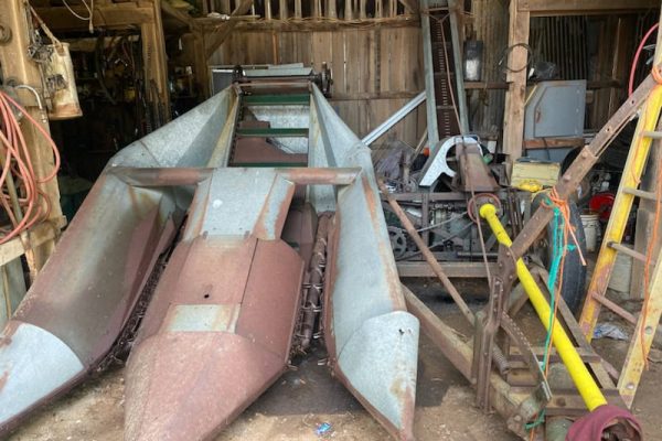 Rusty vintage farm equipment with metal frame and blades in barn setting.
