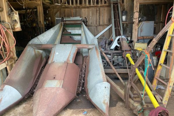 Rusty vintage farm equipment with metal frame and blades in barn setting.