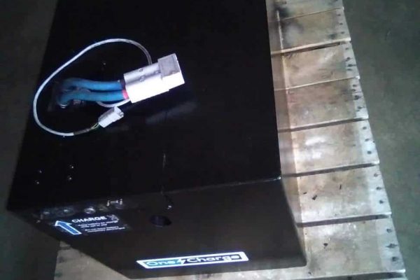 Large black industrial battery pack with wiring on wooden pallet in warehouse.