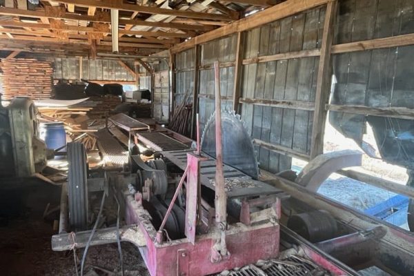 Old sawmill machinery with rust and wear in rustic barn setting.