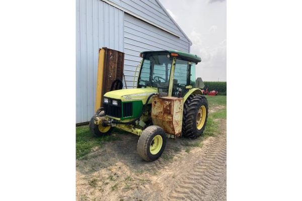 John Deere 5075E tractor from 2018 with front loader attachment, parked beside a blue barn on a farm.