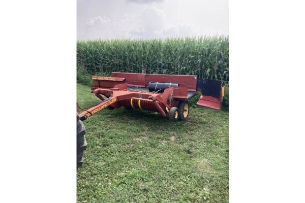 Red agricultural rotary cutter attached to a tractor, used for mowing and land clearing, on a grassy field near a cornfield.