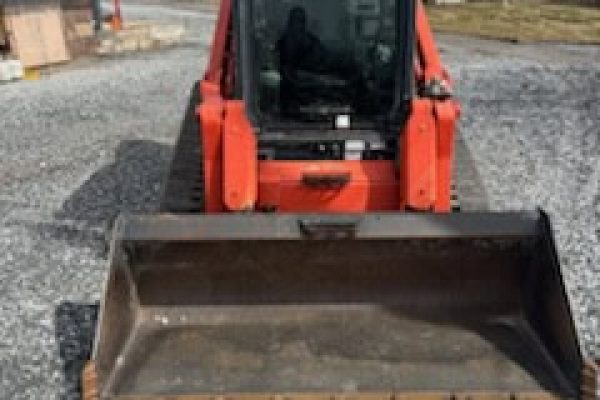 Excavator with a front bucket attachment, orange and black, parked on gravel surface outdoors.
