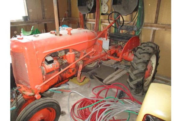 Vintage orange tractor in a barn with tools and equipment, no visible year or model.