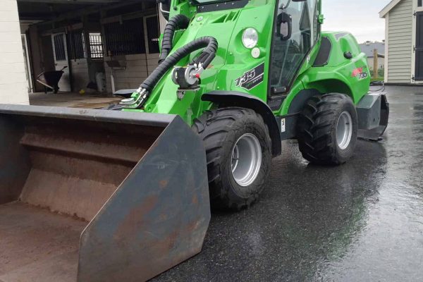 Green compact loader with front bucket, ideal for construction and landscaping projects.