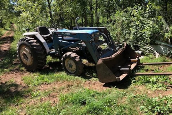 Ford 1920 compact utility tractor with front loader and cab, parked on grassy area near trees.