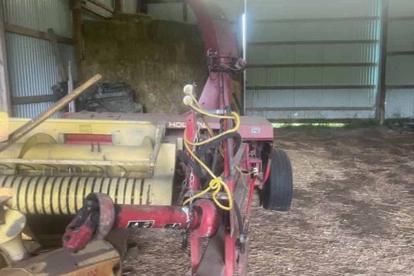 New Holland 782 forage harvester attachment inside barn with metal roof and dirt floor.