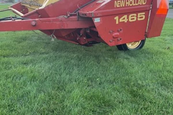 New Holland 1465 haybine with red body and yellow cutting reel on green field.