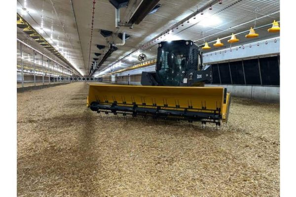 A modern indoor agricultural facility with a large yellow and black tractor equipped with a front-mounted blade.