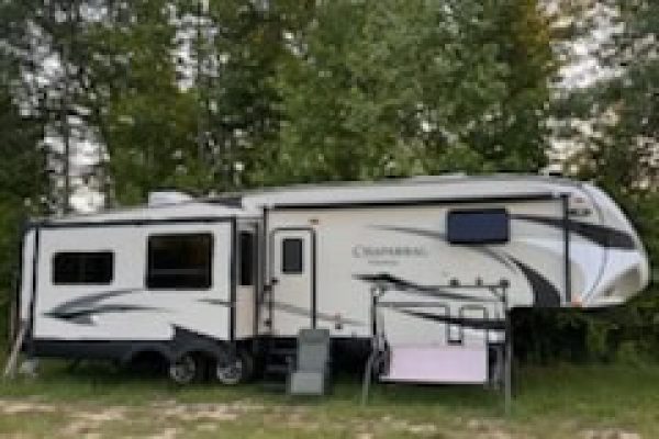 2021 Chamberlain fifth wheel RV with slide-outs and modern exterior design, parked on grassy area with trees in background.