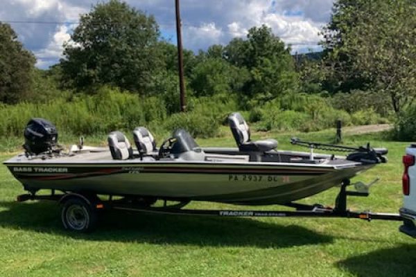Bass Tracker fishing boat with three outboard motors on a trailer in a grassy field.