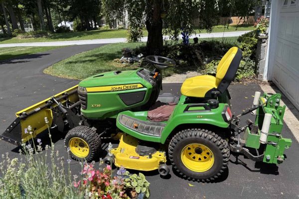 John Deere X730 lawn tractor with front mower deck and snowblower attachment in driveway.