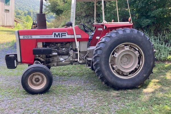 Red Massey Ferguson 215 tractor with canopy, large rear tires, and open engine compartment on grassy field.