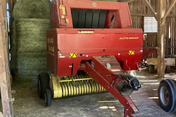 Red Auto-Wrap hay baler with yellow pickup in a barn setting.