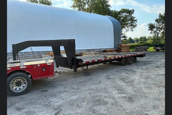 2018 BWise gooseneck tilt trailer with red cab and long flatbed, dual rear axles, in outdoor lot.
