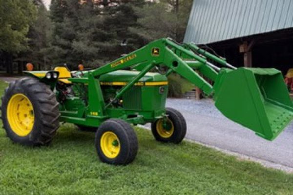 Green John Deere 2440 compact tractor with front loader and yellow wheels on grassy area.