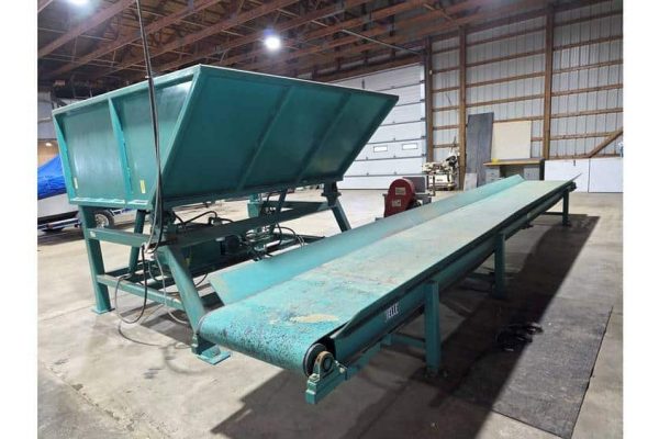 A conveyor belt system with a tilting hopper in an industrial warehouse setting.