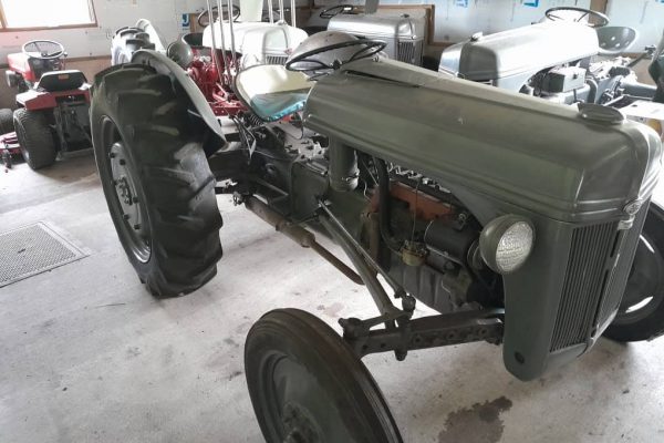 1939 Ford 9N vintage tractor with large rear tires and metal hood in indoor storage.
