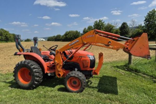 Kubota L3800D compact tractor with front loader, orange color, large rear tires, and enclosed cab, on grassy field.