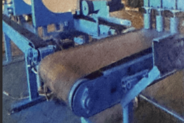 Blue industrial bandsaw with conveyor belt and control panel in workshop setting.