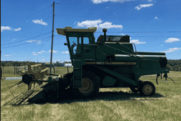 Green John Deere 6600 tractor with mowing attachment on a grassy field under blue sky.