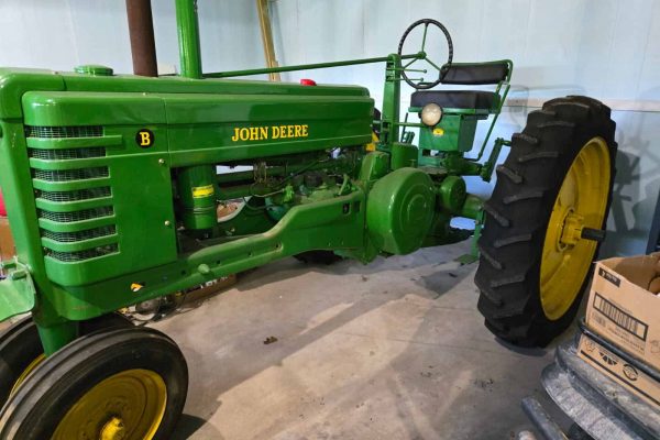 1948 John Deere B tractor with green body and yellow wheels, front grille, and seat in a storage area.