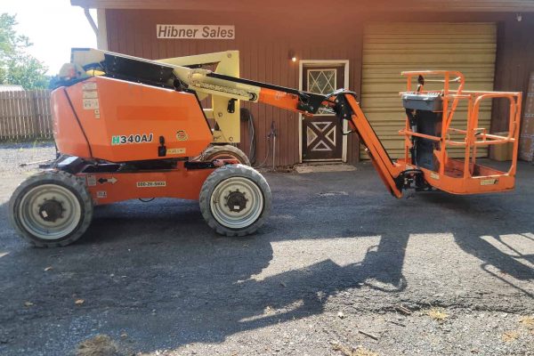 2019 JLG 340AJ boom lift with orange platform and black arm, parked outside a building with Hibner Sales sign.