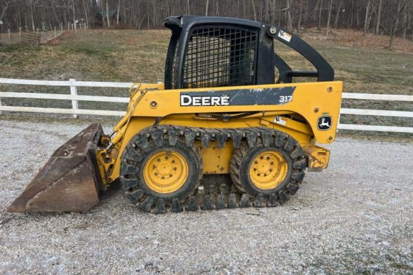 John Deere 317 compact skid steer loader with bucket attachment and enclosed cab.