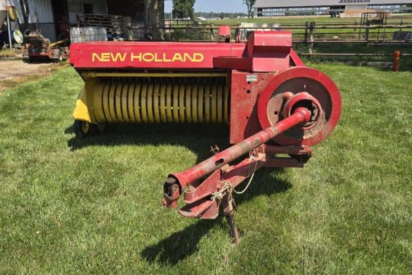 New Holland 273 hay rake with red and yellow color, large wheels, and tines for hay collection.