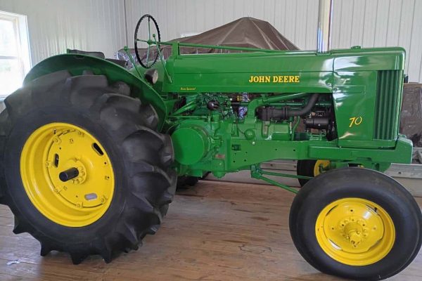John Deere 70 tractor with green body and yellow wheels inside a barn.