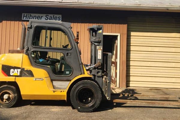 Yellow Caterpillar forklift with black tires parked outside Hibner Sales building.