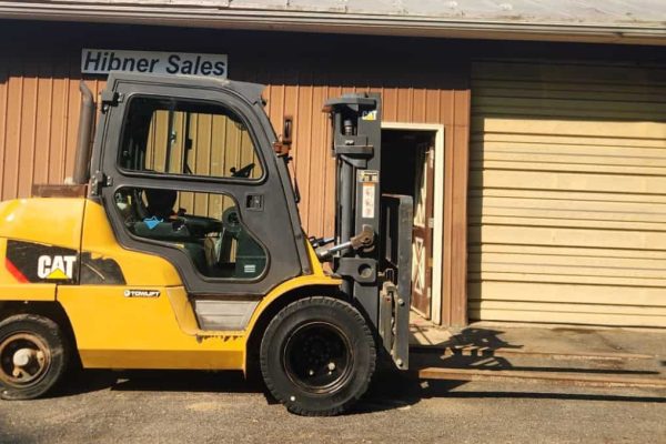 Yellow Caterpillar forklift with black tires parked outside Hibner Sales building.