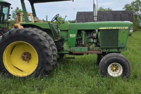 Green John Deere 4620 tractor with canopy and large rear tires on grassy field.