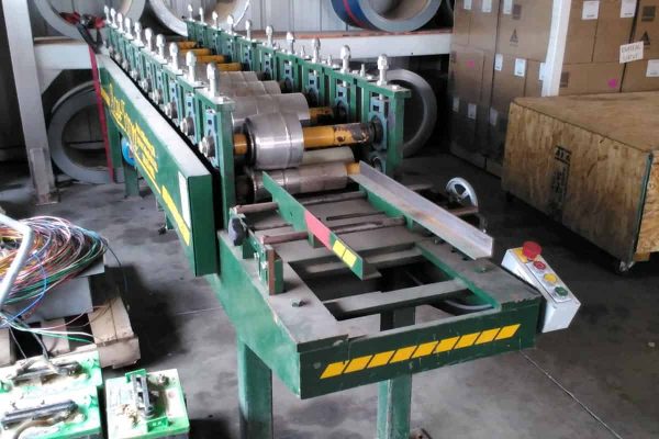 Industrial beaded fascia machine with rollers and control panel in warehouse setting.