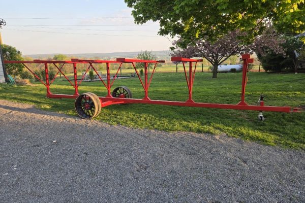 Red tobacco lath trailer with wheels and frame on grassy area under trees.