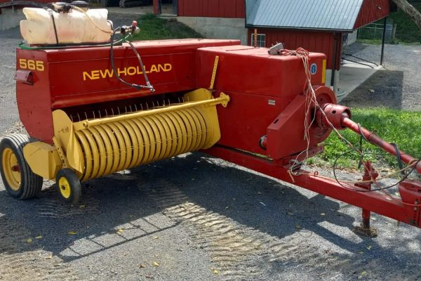 Red New Holland 565 hay conditioner with yellow rollers and hitch for tractor attachment.