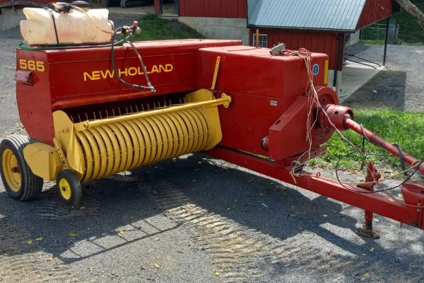 Red New Holland 565 hay conditioner with yellow rollers and hitch for tractor attachment.