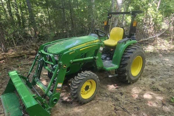 2021 John Deere 3025E compact tractor with front loader and yellow seat in wooded area.