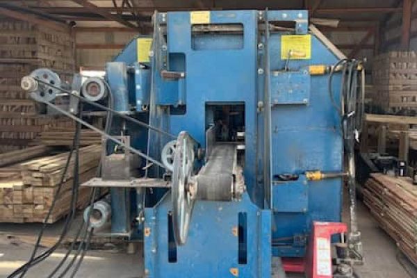 Industrial metalworking machine in a warehouse, blue color, with rollers and control panels.