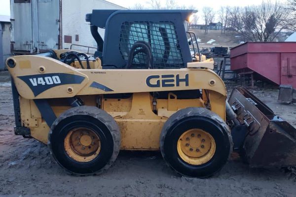 Vibrant yellow GEH V400 skid steer loader with bucket attachment, parked outdoors on a farm or construction site.