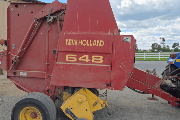 New Holland 648 round baler in red with yellow wheels and branding.