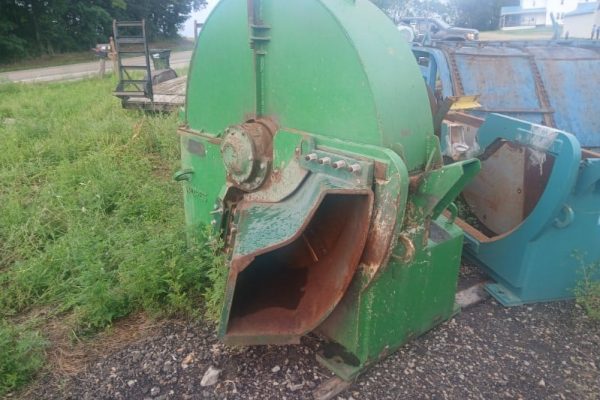 Green industrial wood chipper with rusted intake chute and worn paint, outdoor setting.