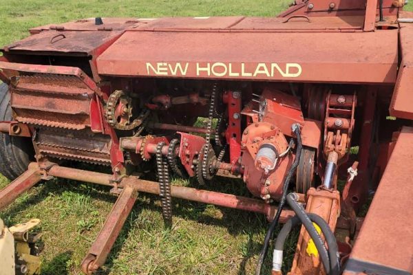 Old New Holland tractor with visible tracks and mechanical parts, red paint, and signs of wear.