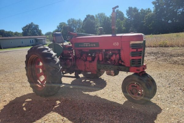 Red Farmall 450 tractor with large rear tires and smaller front tires on gravel surface.