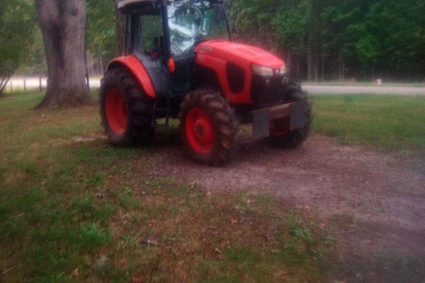 Red Kubota M5-111 compact tractor with cab and large tires in a grassy area.