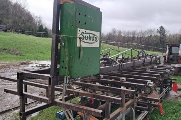Agricultural equipment with green and black components, including a tractor and conveyor system, on a farm field in rural set.