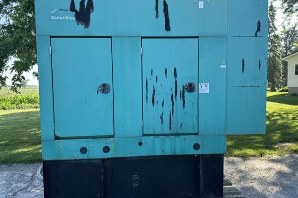 Blue industrial generator with visible rust and wear, outdoors on a concrete pad.
