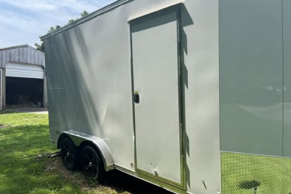 Green enclosed aluminum concession trailer with side door and dual axles on grassy area.