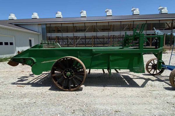 Vintage green manure spreader with large wooden wheels and metal frame.