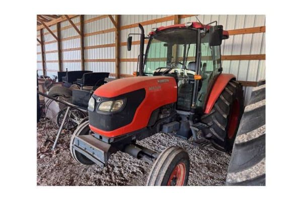 Red Mahindra tractor with enclosed cab and front loader attachment in a barn setting.